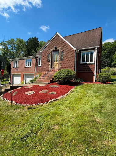 Red mulch bed with a stone border and flagstone stepping stones in front of a brick home