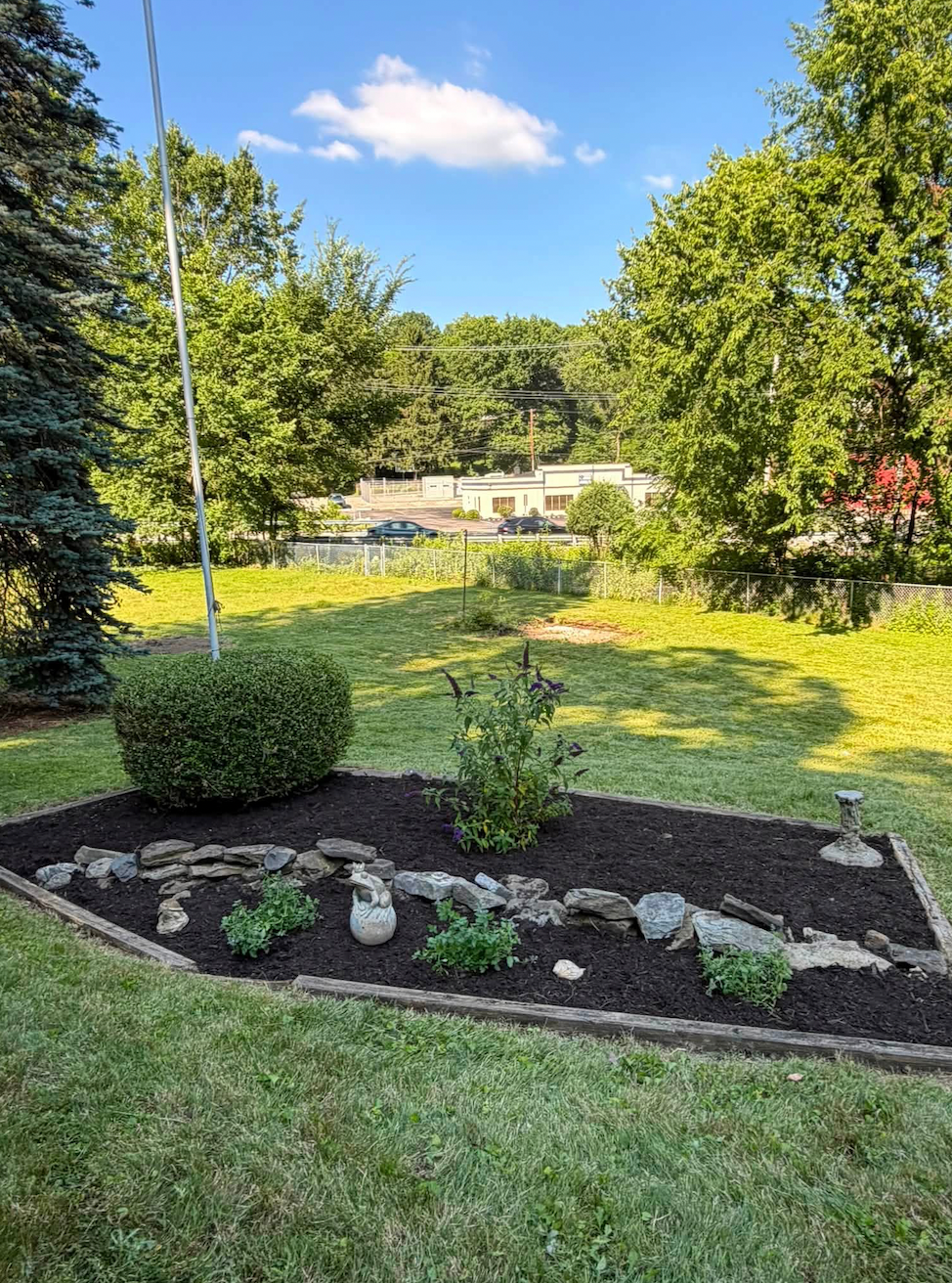 Defined mulch bed with timber edging, stone accents and new plantings around a flag pole