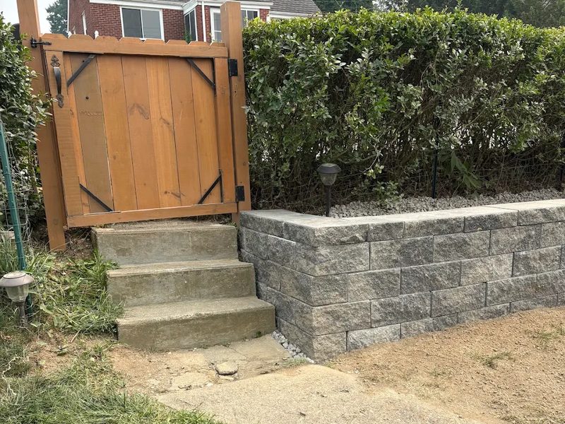 Gray block retaining wall with capstone beside concrete steps and a wooden gate