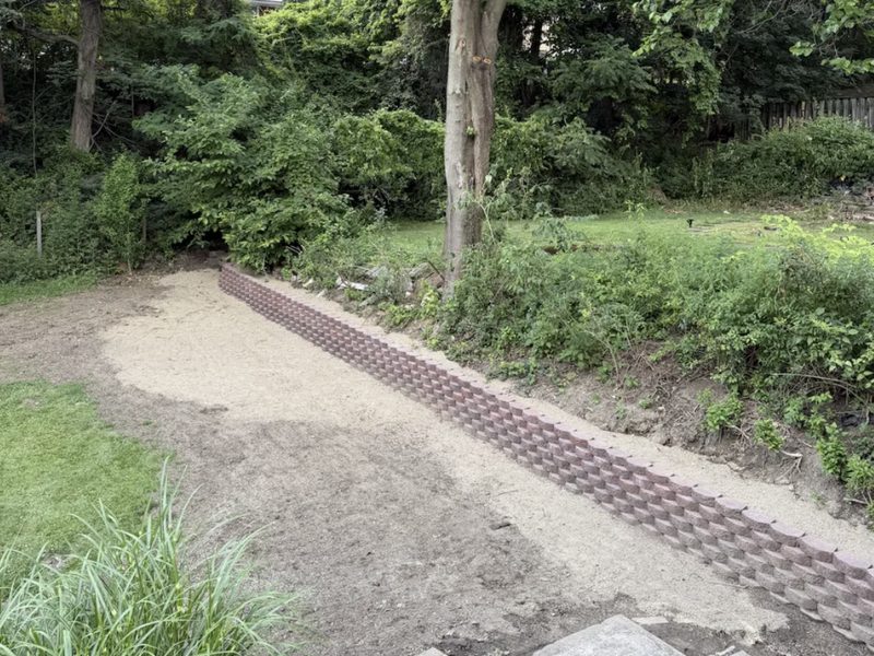 Curved brown block retaining wall terracing a wooded backyard slope