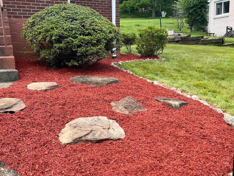 Red mulch bed with flagstone stepping stones and a rounded river rock border
